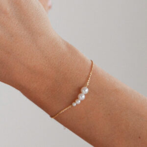 Mulher usando pulseira minimalista em ouro rosé 18k com quatro pérolas brancas naturais