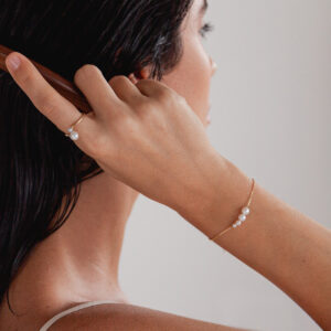 Mulher usando anel e pulseira feita a mão em ouro 18k com pérolas brancas naturais de tamanhos diferentes