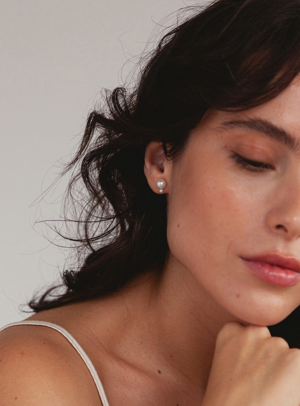 mulher usando brinco de pino minimalista feito à mão em ouro 18k com duas pérolas brancas naturais de diferentes tamanhos