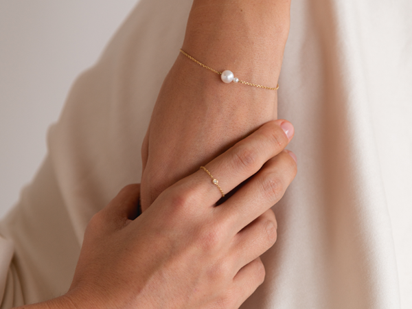 mulher com a mão apoiada na perna usando anel e pulseira feitos à mão em ouro 18k com diamante e pérolas brancas naturais