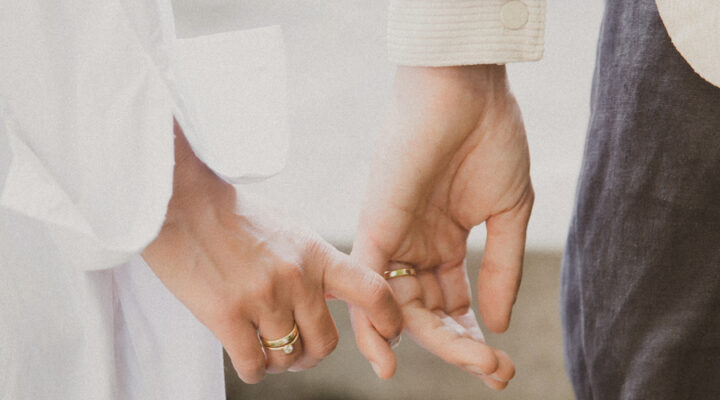 casal usando par de alianças para casamento e anel de noivado feitas em ouro 18k de aro largo e polido com diamante