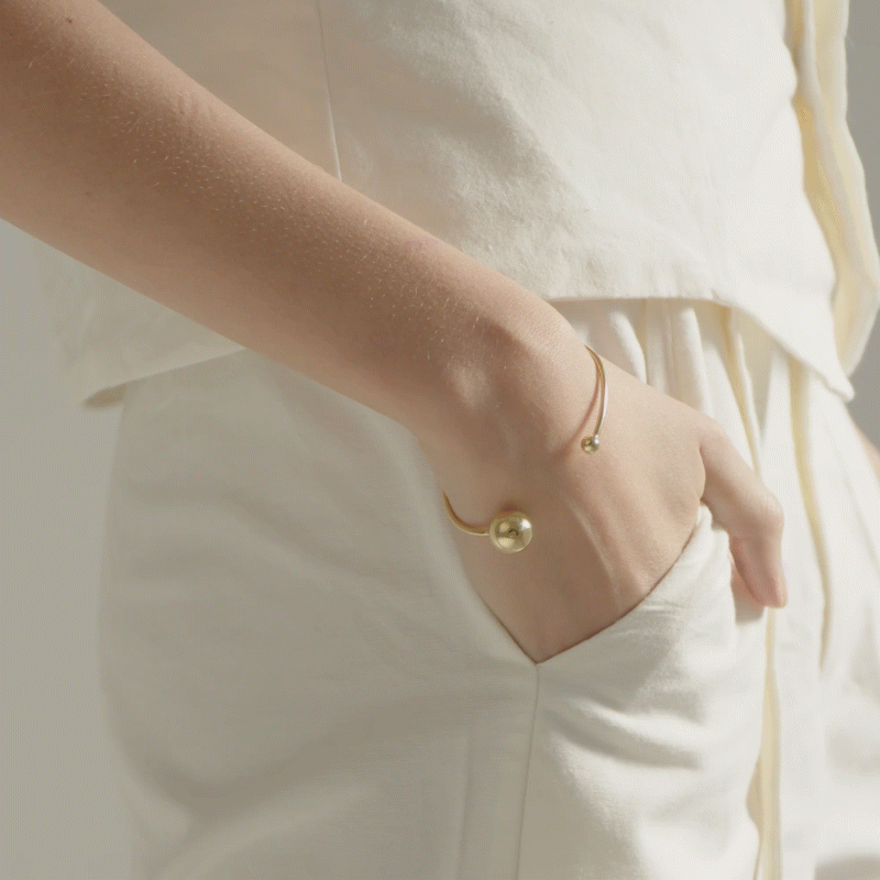 mulher usando bracelete minimalista feito a mão em ouro 18k com duas esferas na ponta do aro