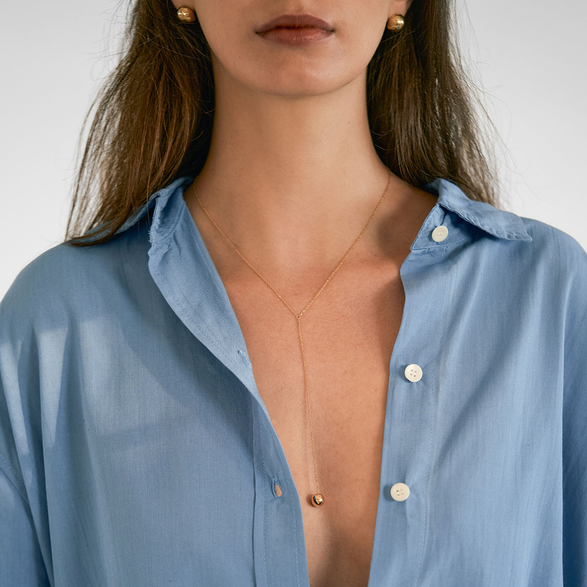 Mulher de blusa azul usando colar feito a mão em ouro 18k de corrente cartier fina com esfera na ponta
