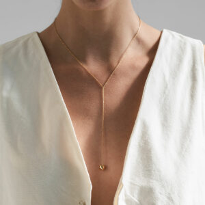 Mulher de blusa branca com decote usando colar feito a mão em ouro 18k de corrente cartier fina com esfera na ponta