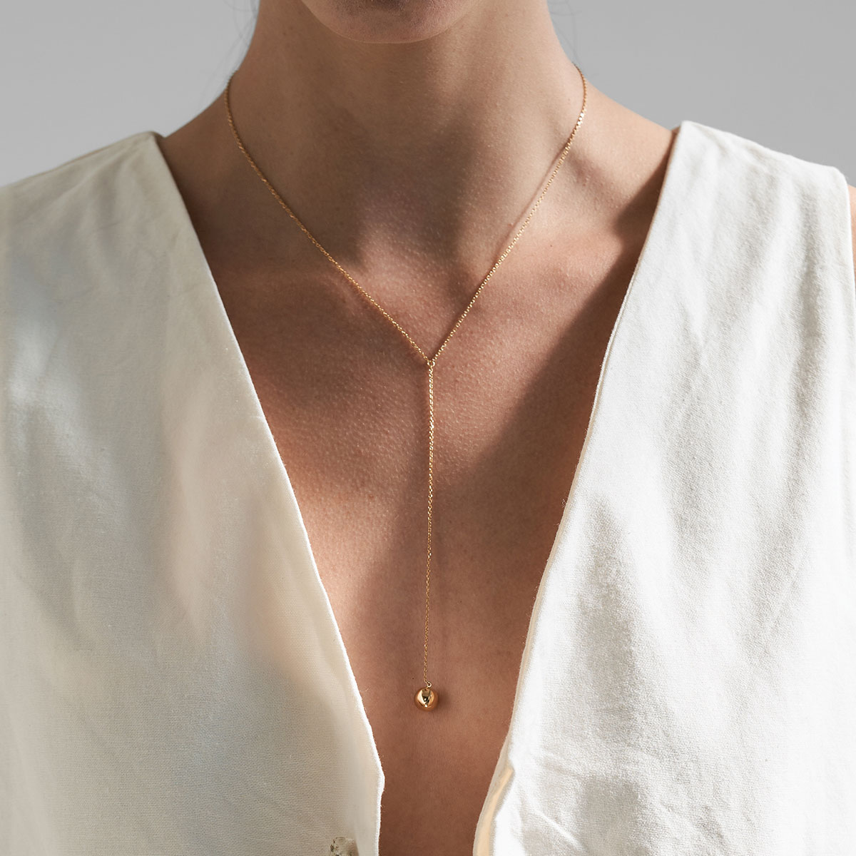 Mulher de blusa branca com decote usando colar feito a mão em ouro 18k de corrente cartier fina com esfera na ponta