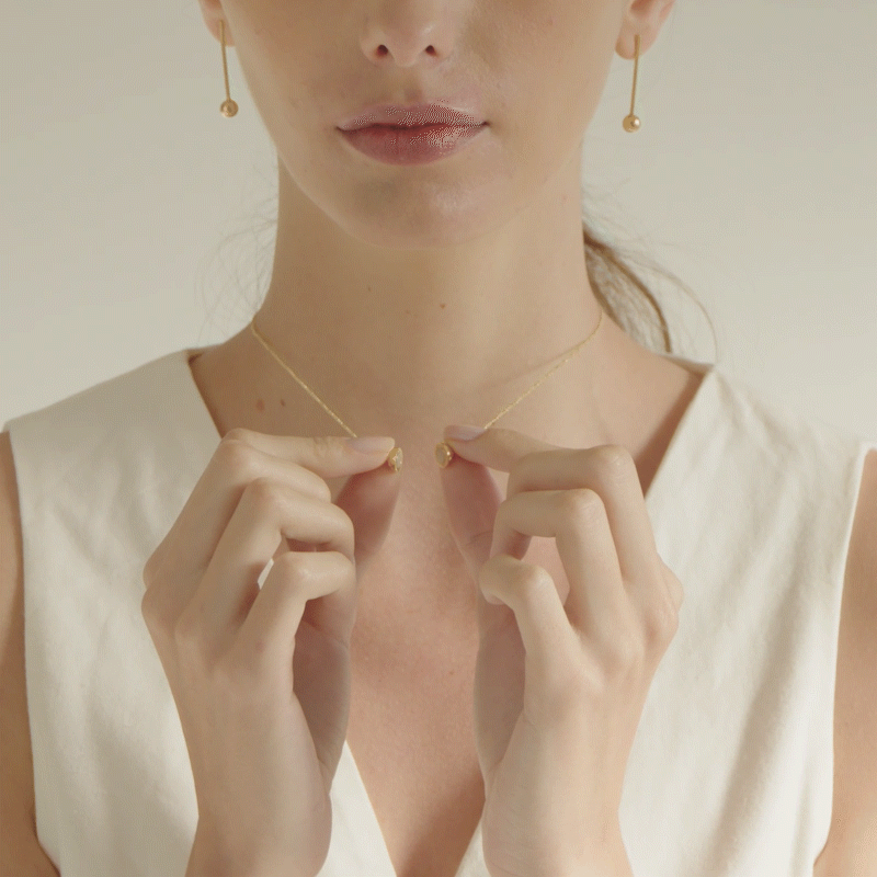 mulher fechando colar minimalista com fecho esférico magnético feito a mão em ouro 18k usando blusa branca com decote