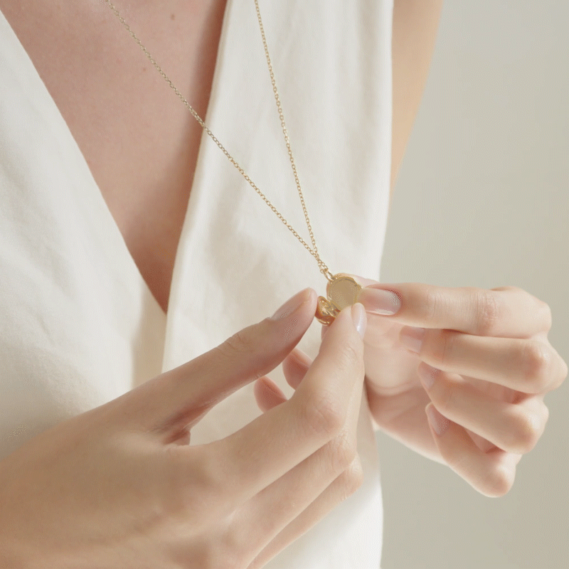 mulher de cabelos longos e soltos segurando colar relicário minimalista feito a mão em ouro 18k para colocar fotos