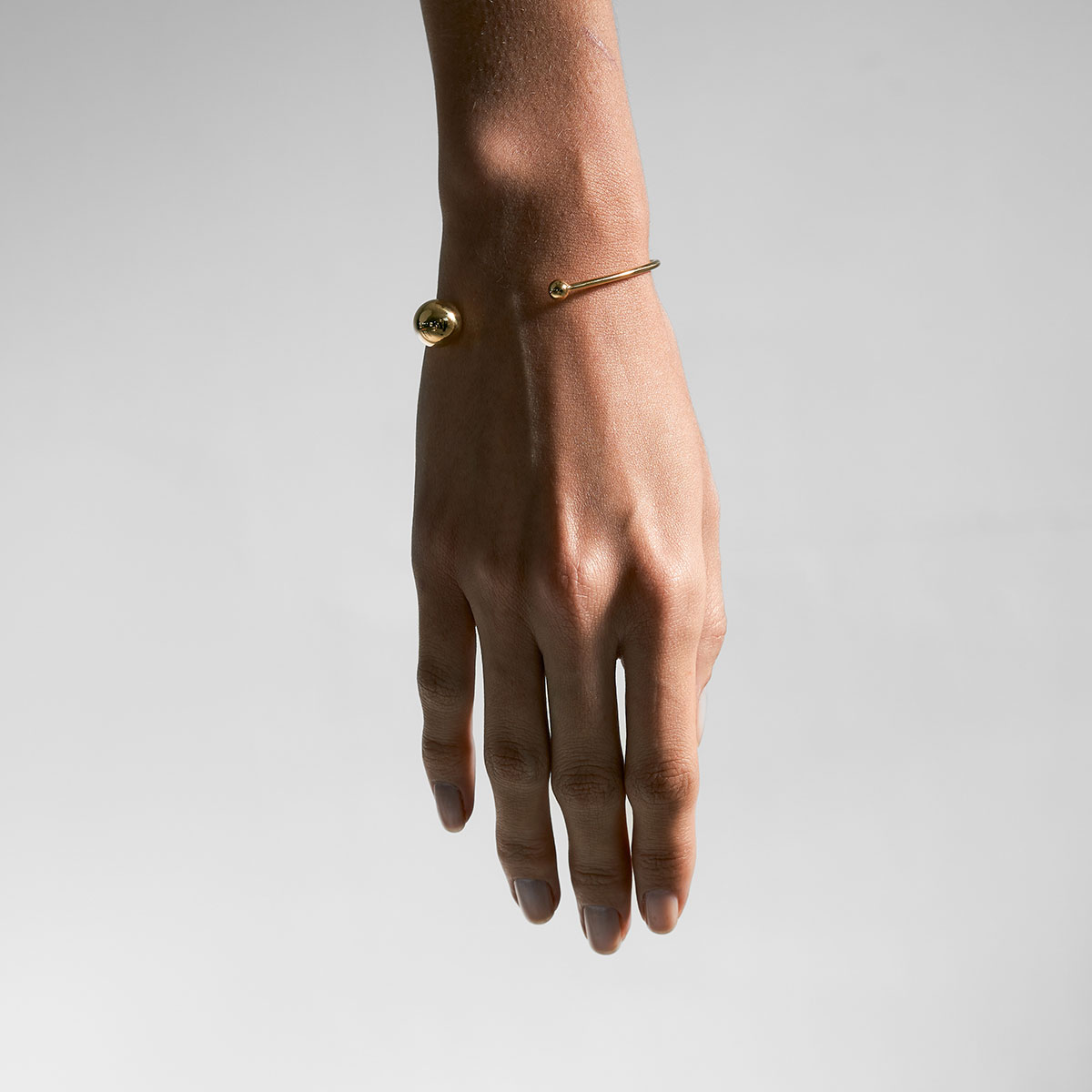 mulher usando bracelete minimalista feito a mão em ouro 18k com duas esferas na ponta do aro
