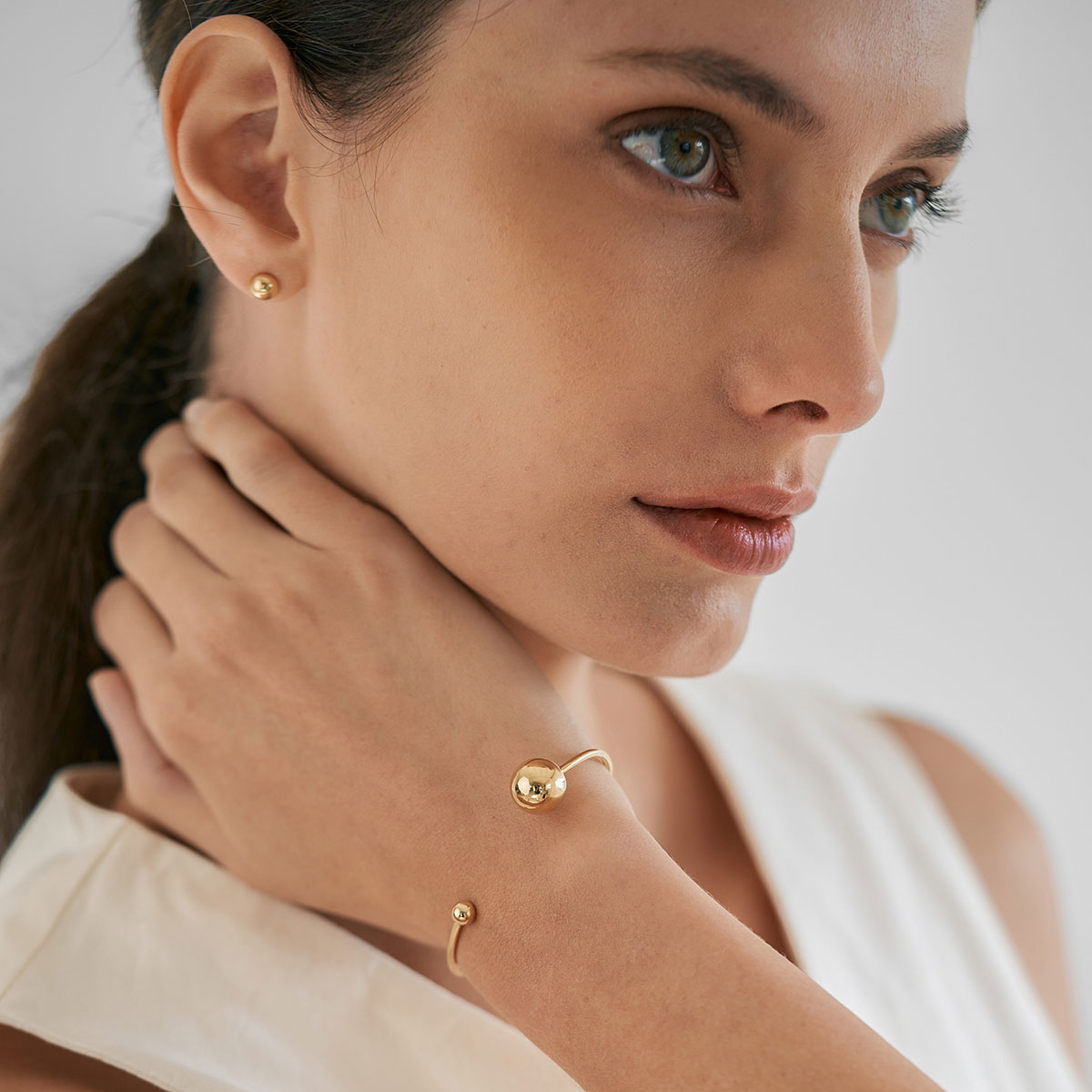 mulher usando bracelete minimalista feito a mão em ouro 18k com duas esferas na ponta do aro