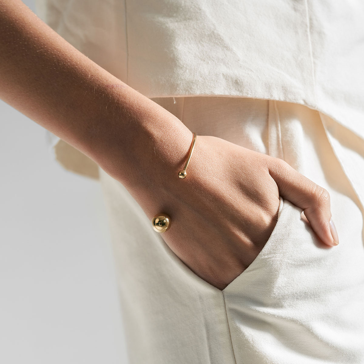 mulher usando bracelete minimalista feito a mão em ouro 18k com duas esferas na ponta do aro