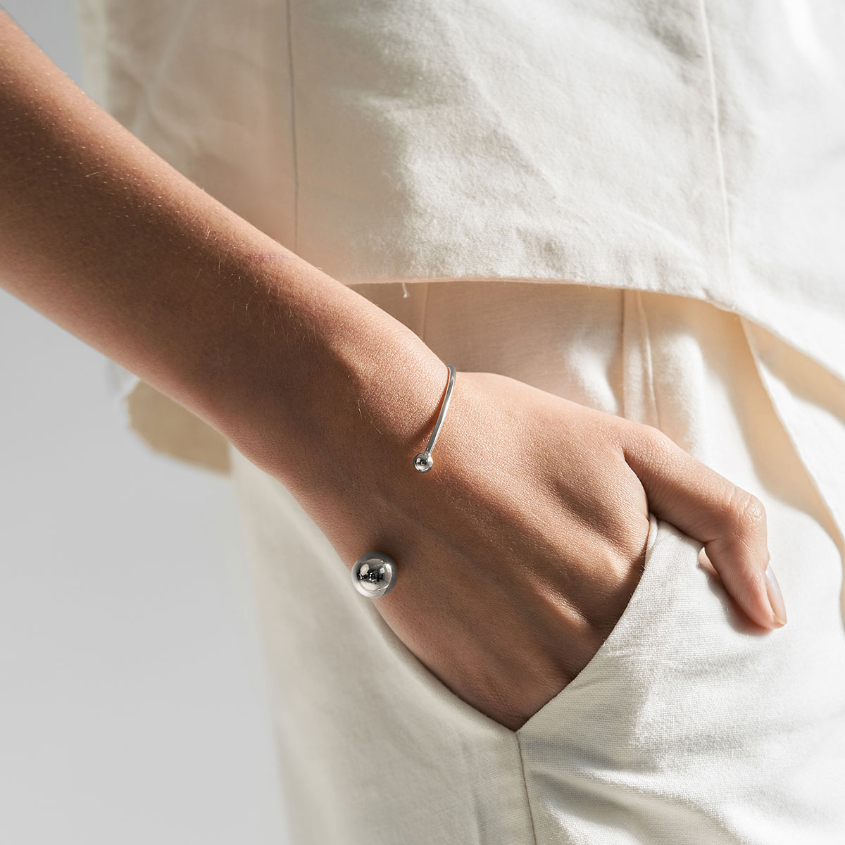 mulher usando bracelete minimalista feito a mão em ouro 18k com duas esferas na ponta do aro