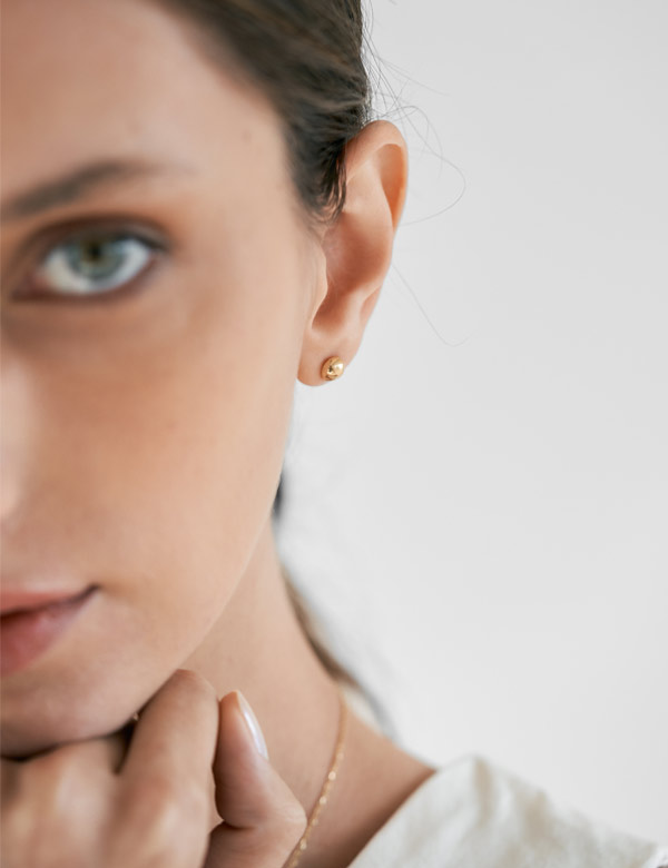 Mulher usando brinco feito a mão em ouro 18k em formato de meia esfera pequena minimalista.