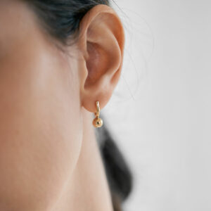 mulher usando brinco de argola minimalista feito a mão em ouro 18k com esfera