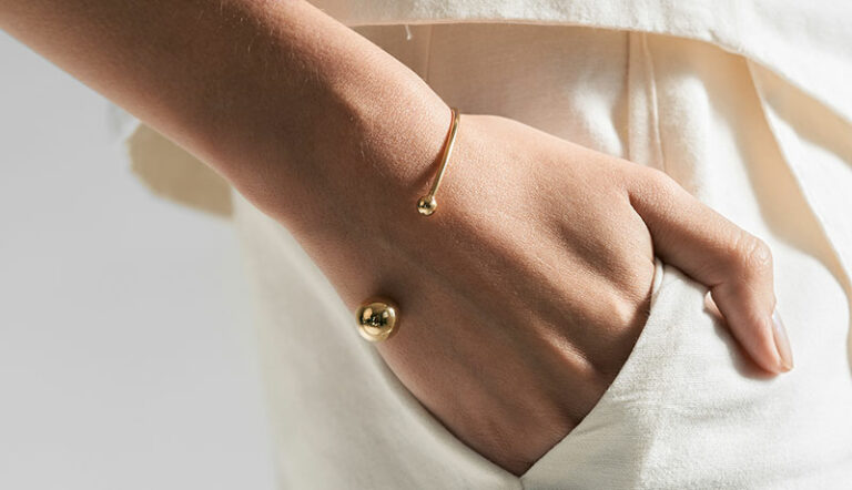 mulher usando bracelete minimalista feito a mão em ouro 18k com duas esferas na ponta do aro