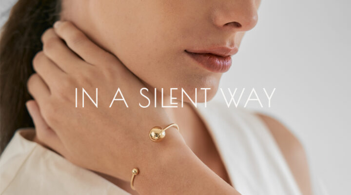Foto de mulher de roupa branca usando bracelete minimalista com esferas de diferentes tamanhos feito a mão em ouro 18k com letreiro escrito "In a Silent Way" em branco