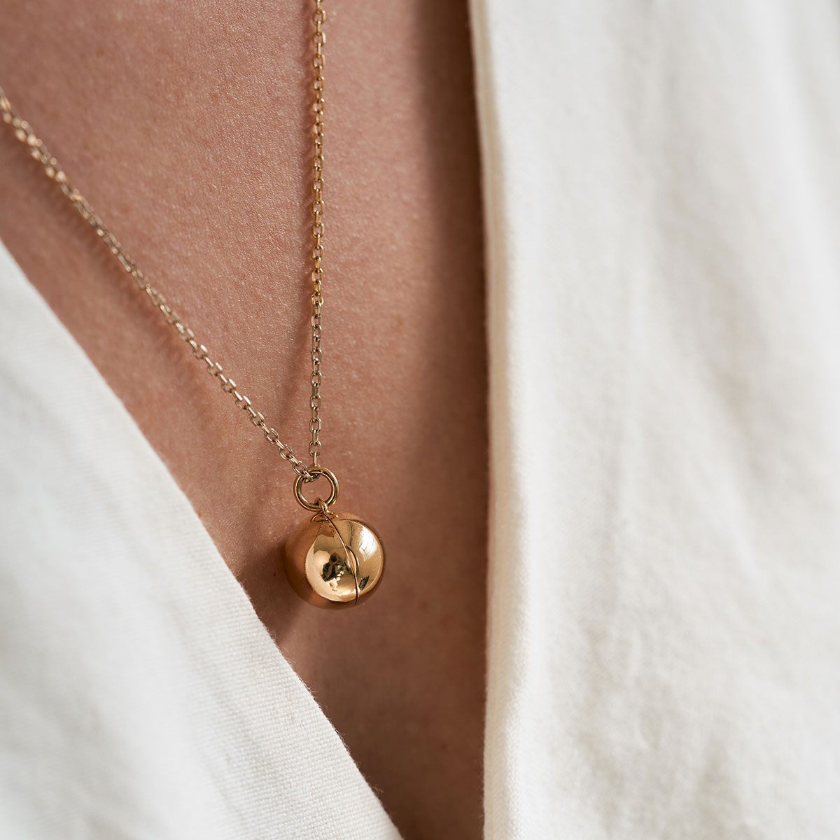 mulher de cabelos longos e soltos usando colar relicário minimalista feito a mão em ouro 18k para colocar fotos
