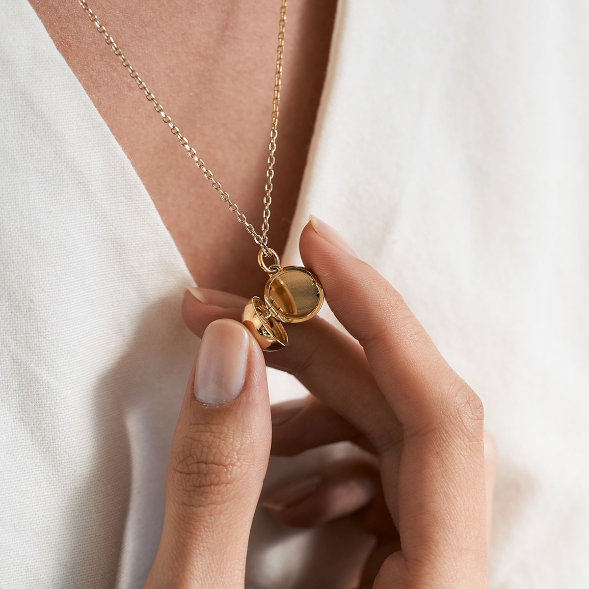 mulher de cabelos longos e soltos segurando colar relicário minimalista feito a mão em ouro 18k para colocar fotos