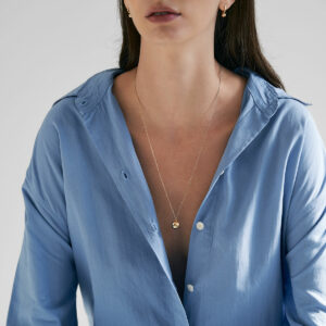 mulher de cabelos longos e soltos usando camisa azul e colar relicário minimalista feito a mão em ouro 18k para colocar fotos