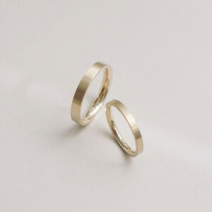 Par de alianças flat em ouro champagne com acabamento fosco acetinado, design minimalista e artesanal.