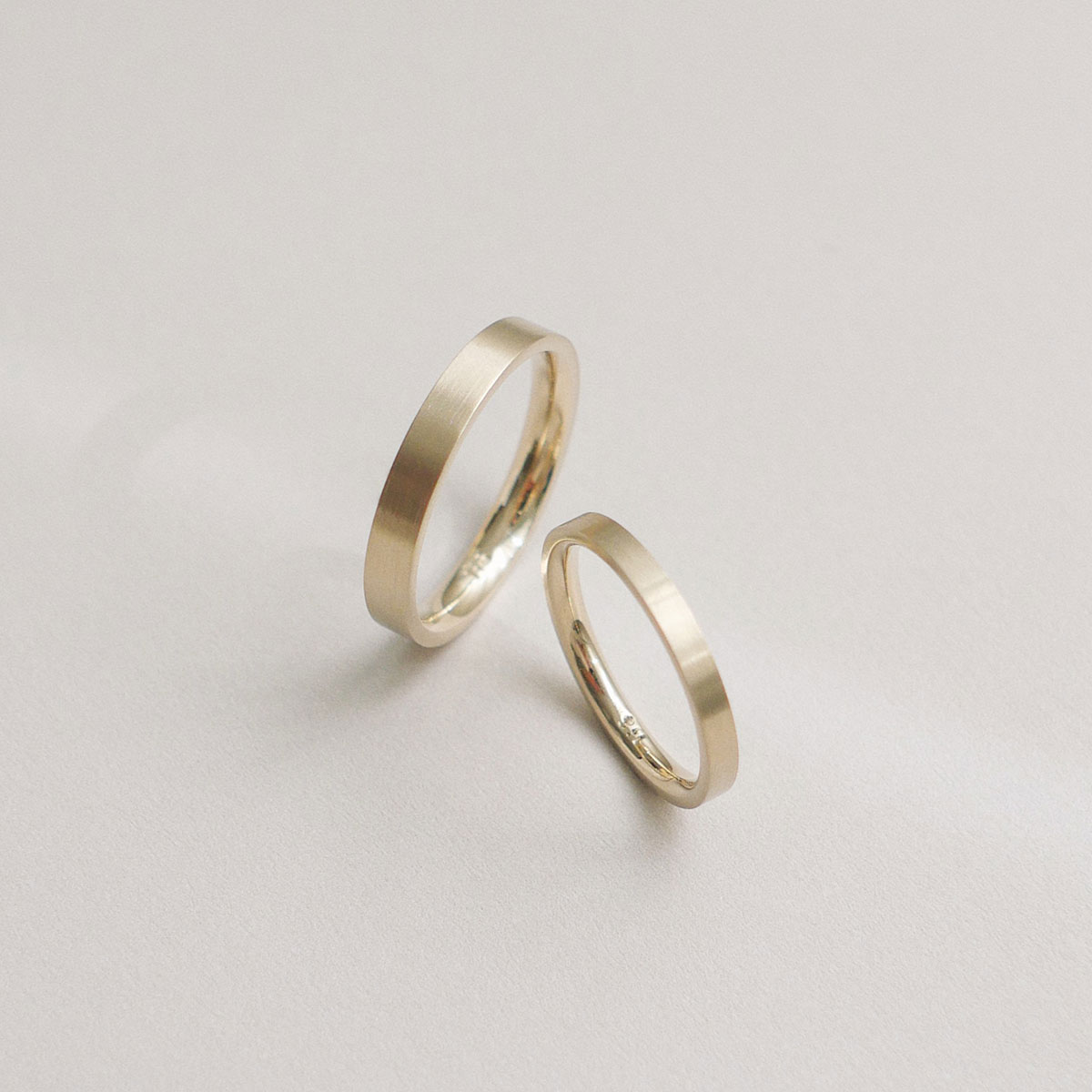Par de alianças flat em ouro champagne com acabamento fosco acetinado, design minimalista e artesanal.