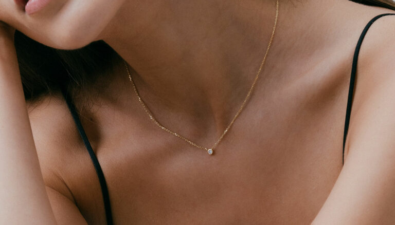 mulher de blusa de alcinhas usando colar minimalista feito à mão em ouro 18k com diamante pequeno e delicado no centro