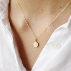 Mulher usando colar com pingente medalha em ouro 18k de acabamento martelado e fosco.