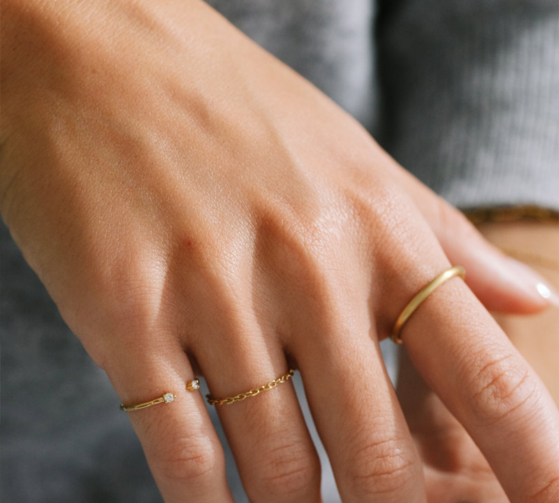 Mão feminina usando anel de corrente, anel aberto com dois diamantes e aliança fosca feitos a mão em ouro 18k.