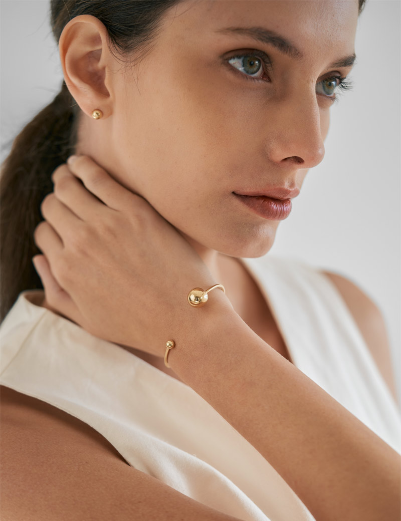 Mulher usando bracelete e brinco esfera pequeno minimalista feito a mão em ouro polido 18k