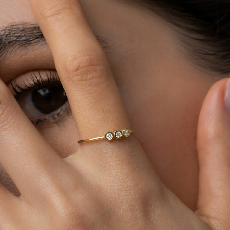 mulher usando anel feito à mão em ouro 18k com três diamantes enfileirados em linha seguindo o aro polido e liso do anel