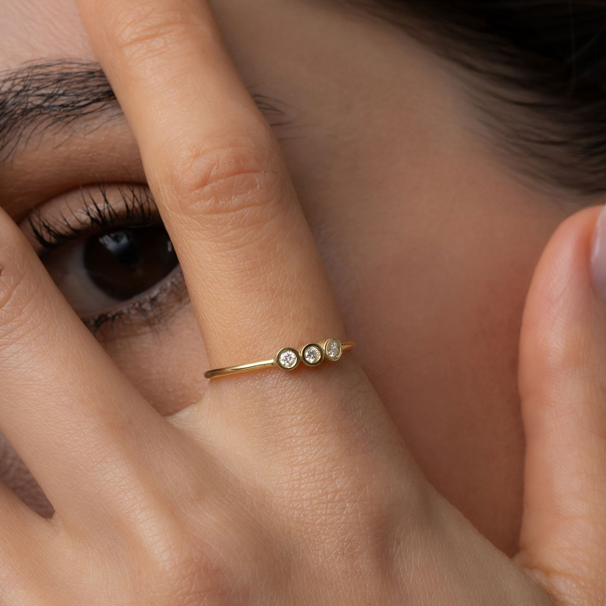 mulher usando anel feito à mão em ouro 18k com três diamantes enfileirados em linha seguindo o aro polido e liso do anel