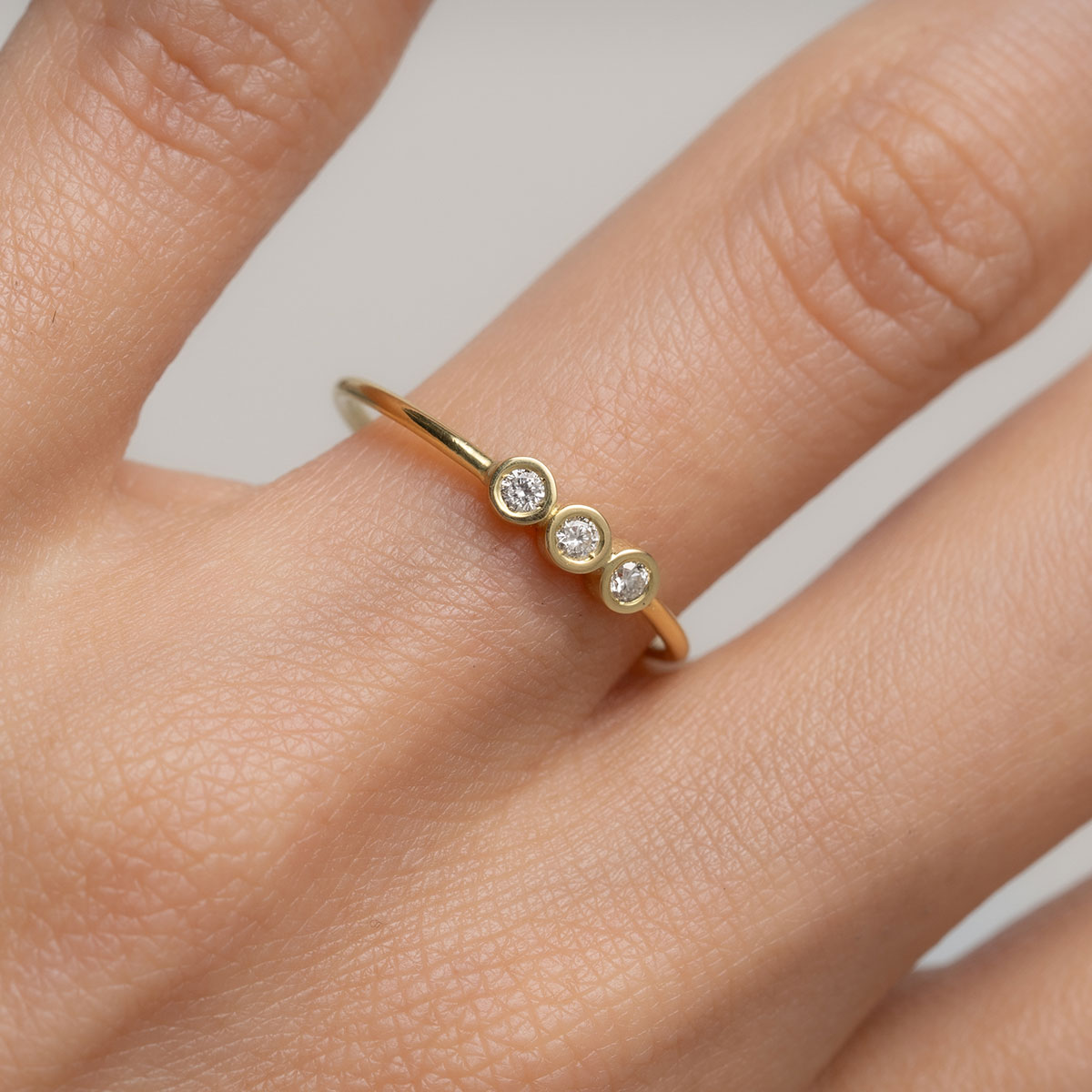 mulher usando anel feito à mão em ouro 18k com três diamantes enfileirados em linha seguindo o aro polido e liso do anel