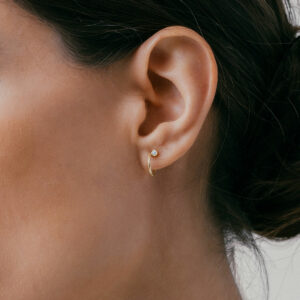 mulher usando brinco de argola minimalista fino com um diamante feito à mão em ouro 18k