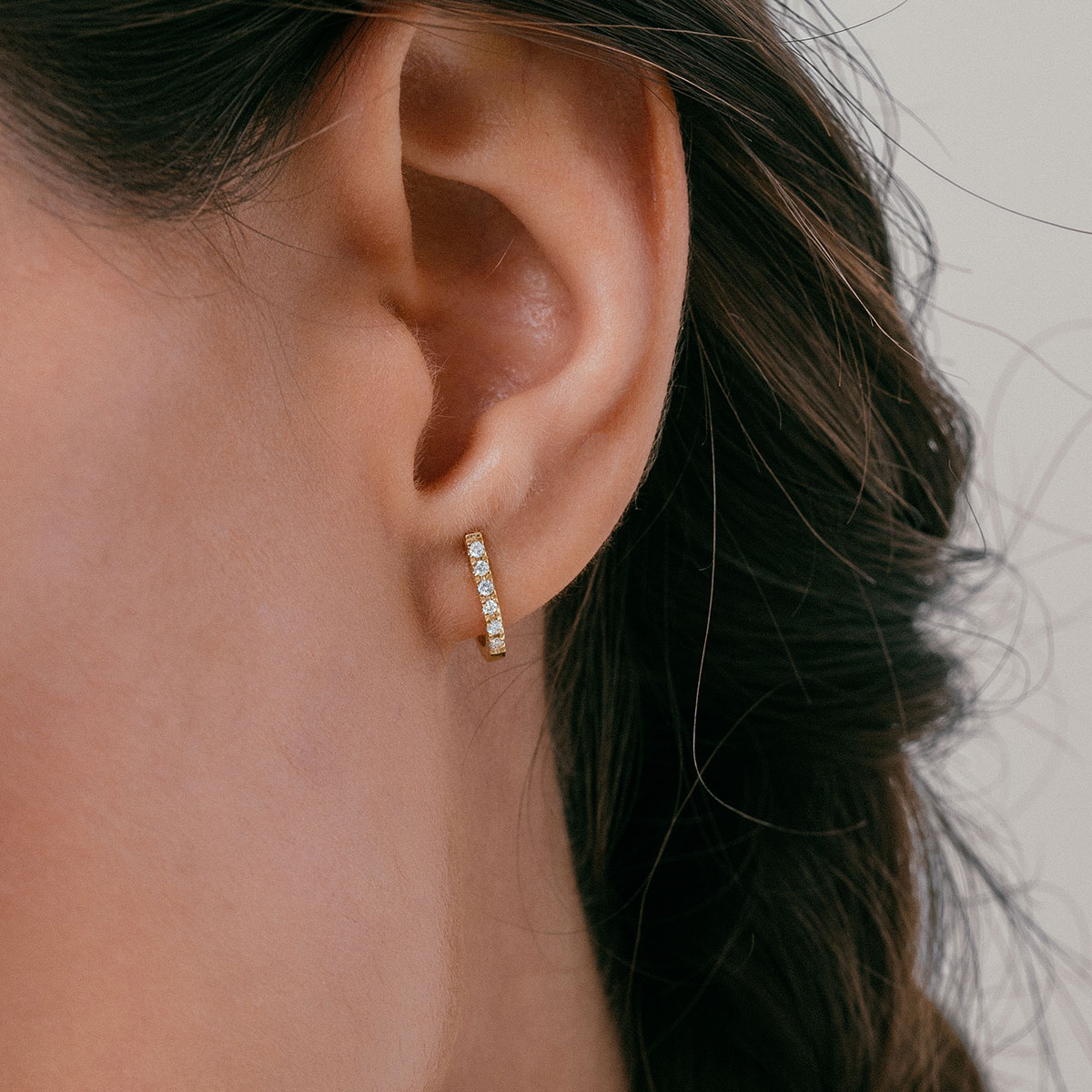 mulher usando brinco minimalista feito à mão em ouro 18k com diamantes que abraça a orelha de forma delicada e sutil