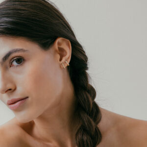 mulher usando brinco minimalista feito à mão em ouro 18k com diamantes que abraça a orelha de forma delicada e sutil