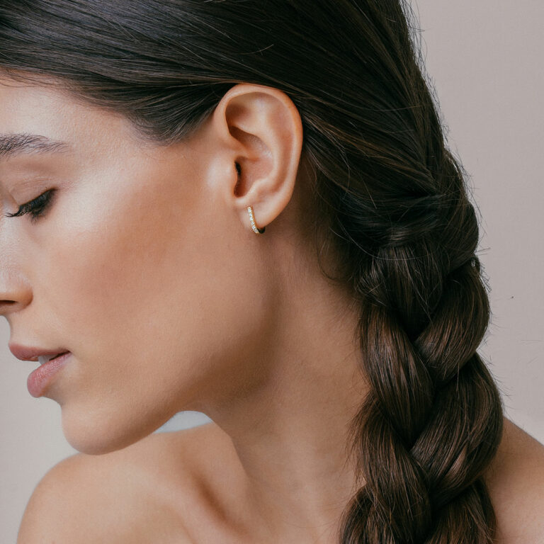 mulher usando brinco minimalista feito à mão em ouro 18k com diamantes que abraça a orelha de forma delicada e sutil