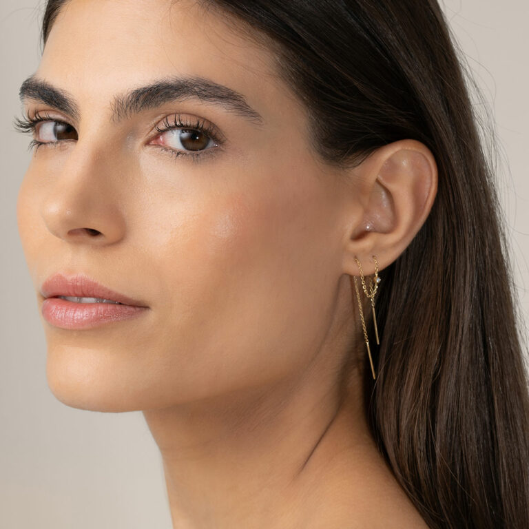 mulher usando brinco longo minimalista de corrente maleável feito à mão em ouro 18k com um diamante delicado