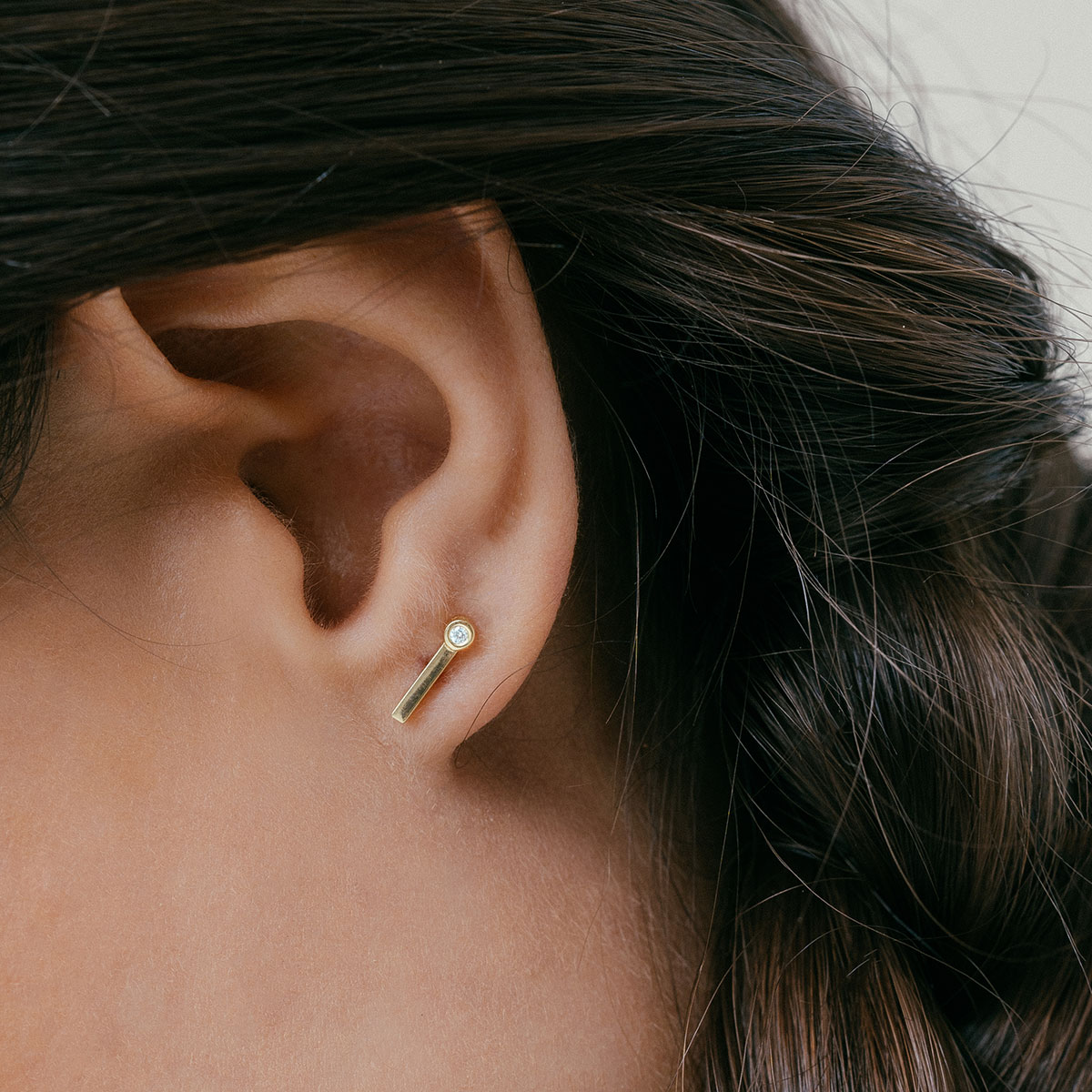mulher usando brinco feito à mão em ouro 18k em formato de palito com um diamante na ponta