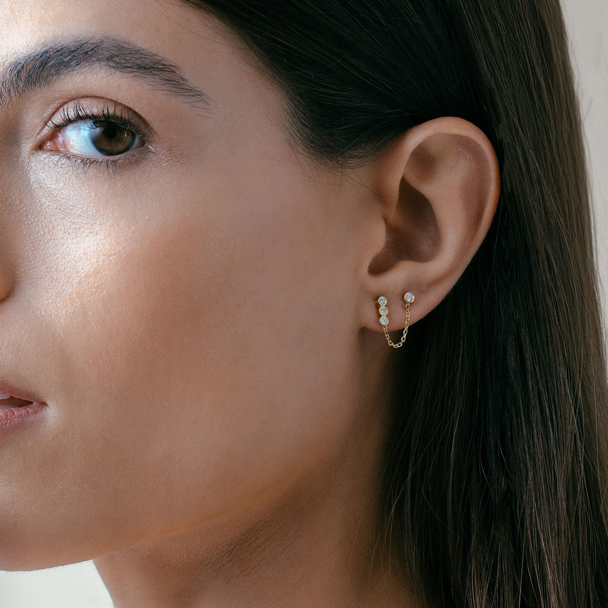mulher usando brinco feito em ouro 18k com três diamantes enfileirados e acessório de corrente