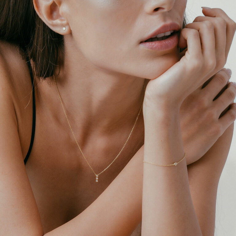 mulher usando pulseira e colar minimalista e delicado feito à mão em ouro 18k com três diamantes enfileirados verticalmente