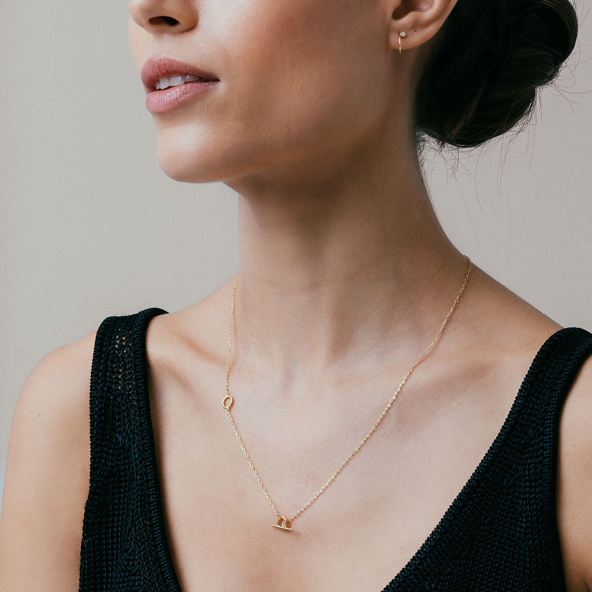 mulher de blusa preta usando colar minimalista de modelo gravatinha com fecho T feito à mão em ouro 18k