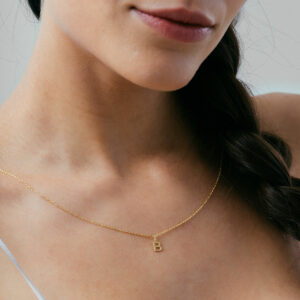 mulher usando colar com pingente minimalista feito à mão em formato de letra e inicial personalizável em ouro 18k