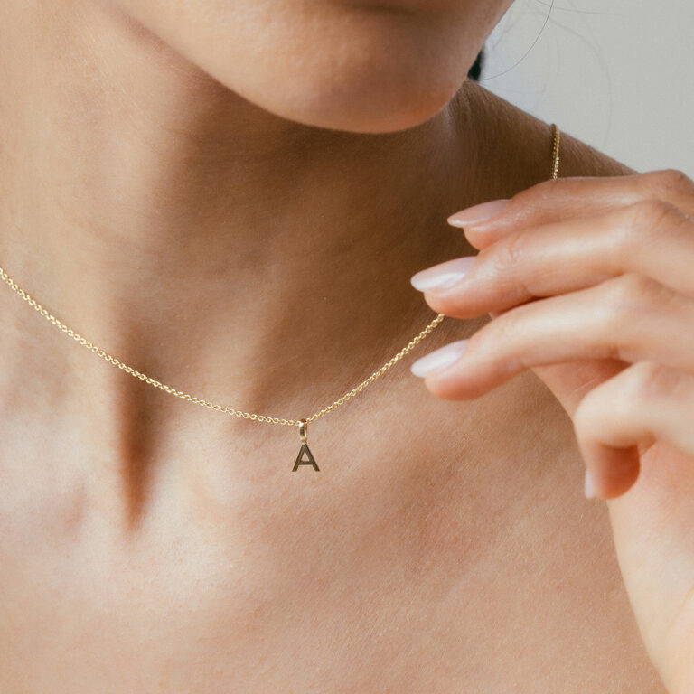 mulher usando colar com pingente minimalista feito à mão em formato de letra e inicial personalizável em ouro 18k