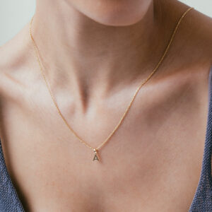 mulher usando colar com pingente minimalista feito à mão em formato de letra e inicial personalizável em ouro 18k