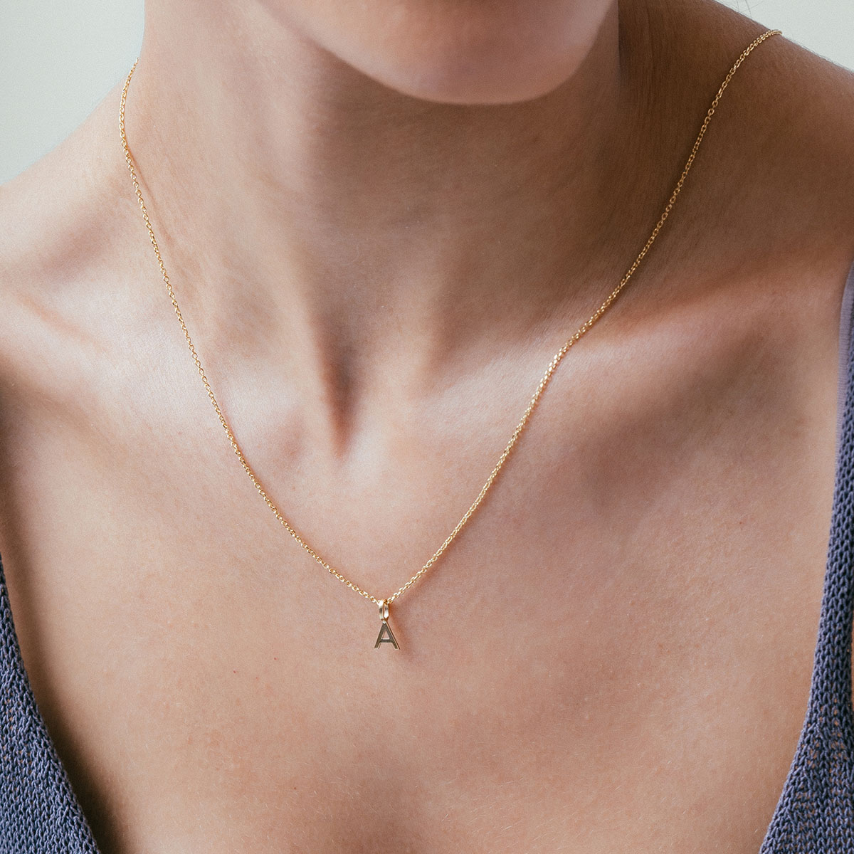 mulher usando colar com pingente minimalista feito à mão em formato de letra e inicial personalizável em ouro 18k