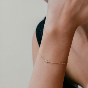 mulher usando pulseira minimalista feita à mão em ouro 18k com diamante ponto de luz central