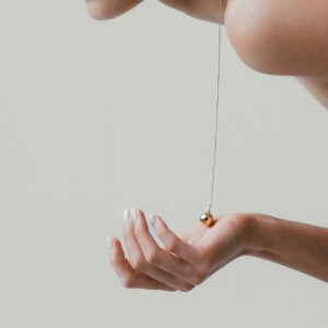 mulher segurando colar com pingente relicário minimalista feito à mão em ouro 18k com diamantes na parte externa e espaço para fotos na parte interna