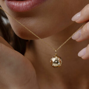mulher segurando colar com pingente relicário minimalista feito à mão em ouro 18k com diamantes na parte externa e espaço para fotos na parte interna