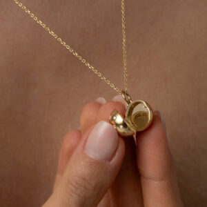 mulher segurando colar com pingente relicário minimalista feito à mão em ouro 18k com diamantes na parte externa e espaço para fotos na parte interna