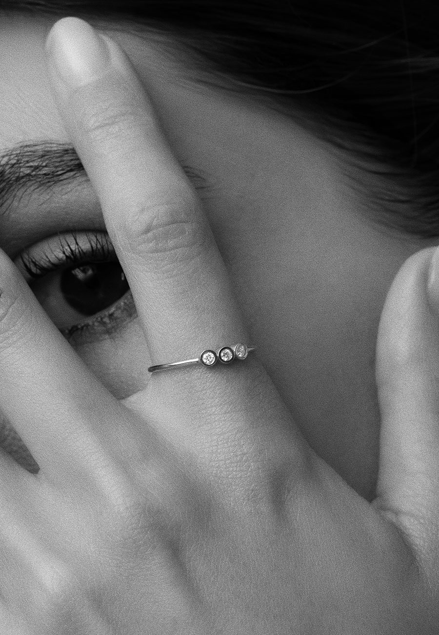 foto em preto e branco de mulher usando anel minimalista e delicado feito à mão em ouro 18k com aro fino e polido e três diamantes do mesmo tamanho alinhados horizontalmente