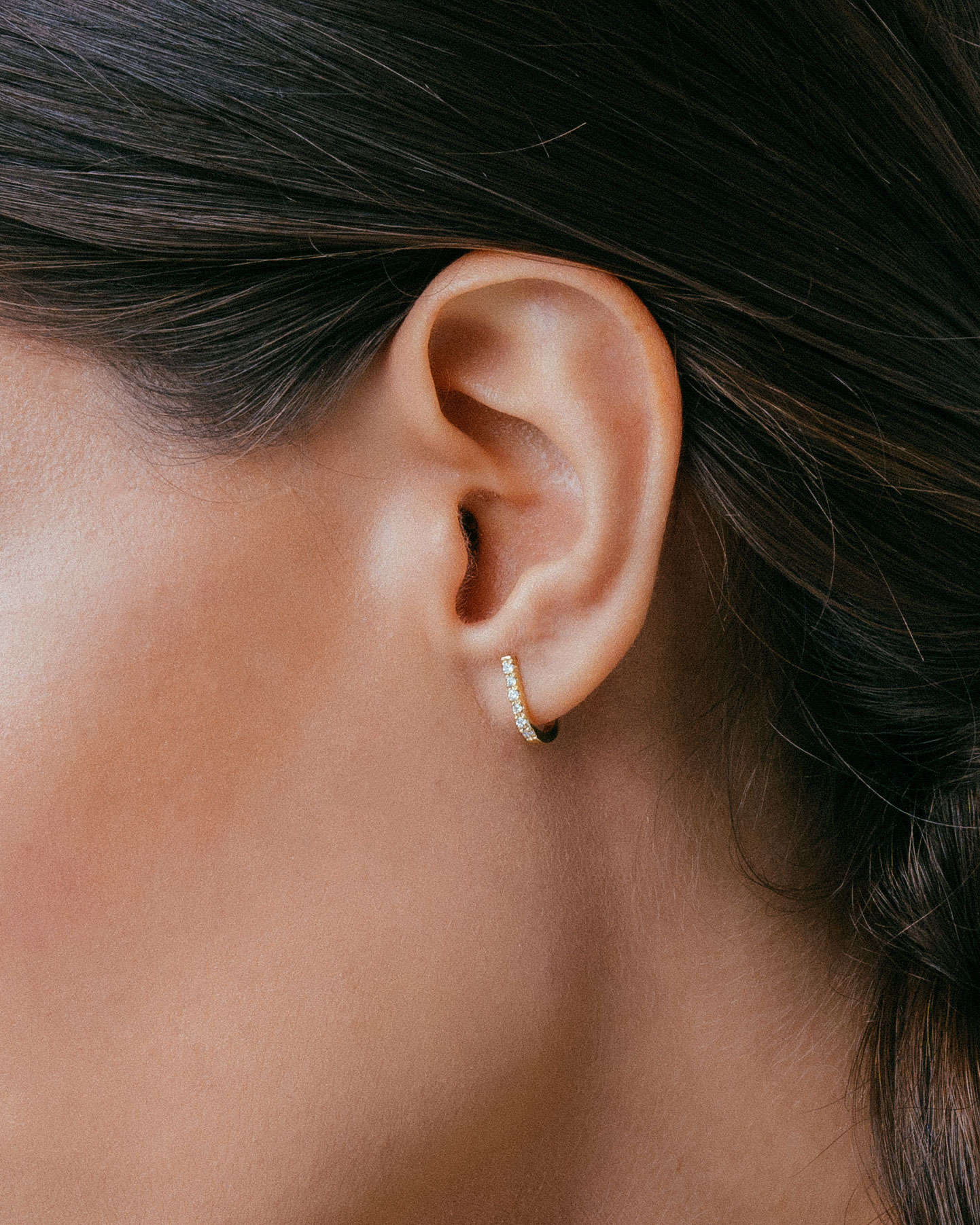 mulher de cabelo castanho usando Brinco minimalista feito à mão em ouro 18k que contorna a orelha com diamantes cravejados na parte da frente